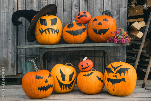 Bright orange pumpkins with painted black faces and bats like jack-o-lanterns on wooden wall background as Halloween's symbols