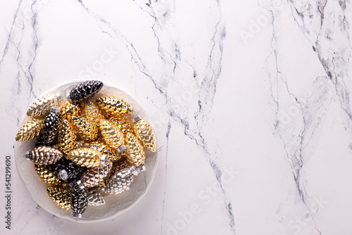 Background with Christmas decorations. Glass gold, black, silver decorative cones on plate on d white marmur  background. Minimalistic style. Still life. Top view.