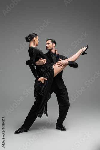 Professional dancers looking at each other while performing tango on grey background