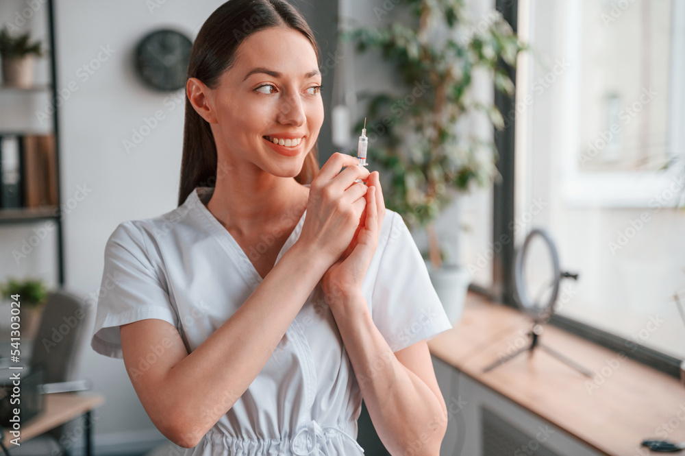 Conception of vaccination. With syringe in hands. Young beautiful female doctor in white coat is in the office Conception of vaccination. With syringe in hands. Young beautiful female doctor in white coat is in the office