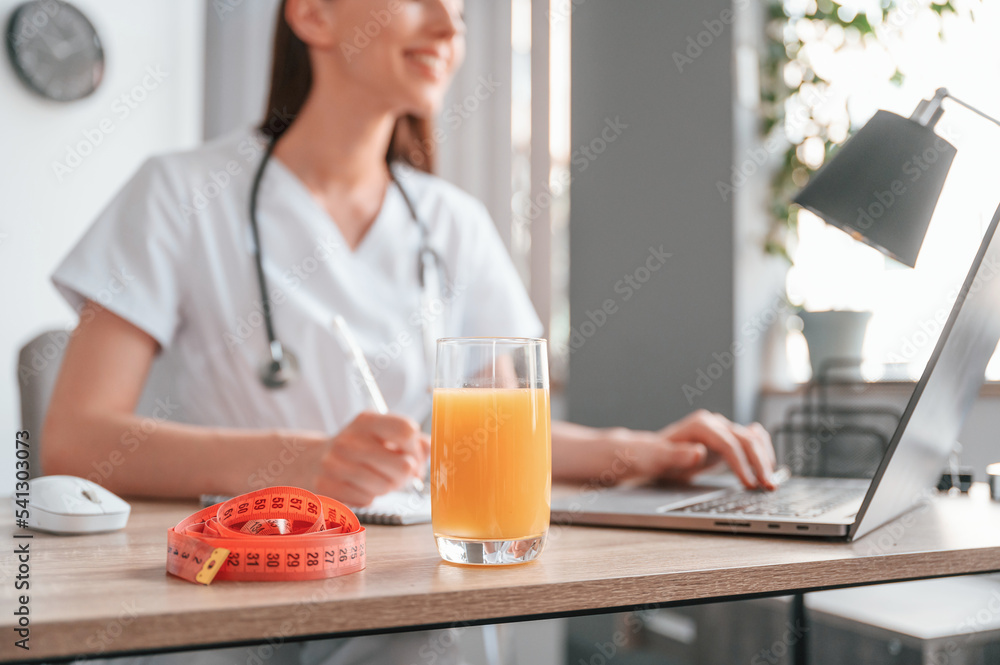 Working by using laptop. Apple juice and measuring length is on the table. Young beautiful female doctor Working by using laptop. Apple juice and measuring length is on the table. Young beautiful female doctor