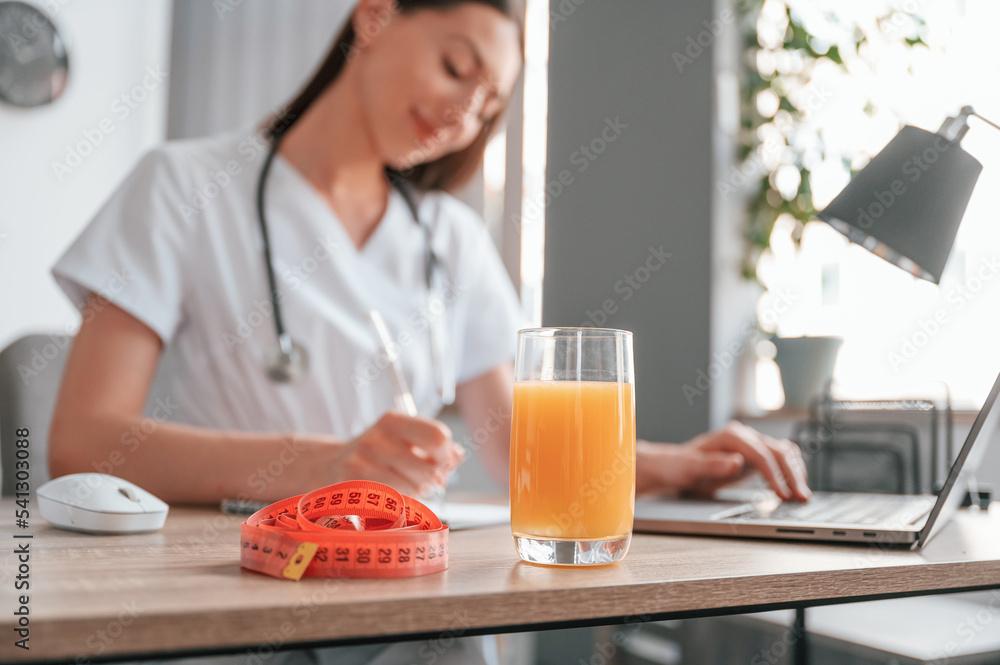 Working by using laptop. Apple juice and measuring length is on the table. Young beautiful female doctor Working by using laptop. Apple juice and measuring length is on the table. Young beautiful female doctor