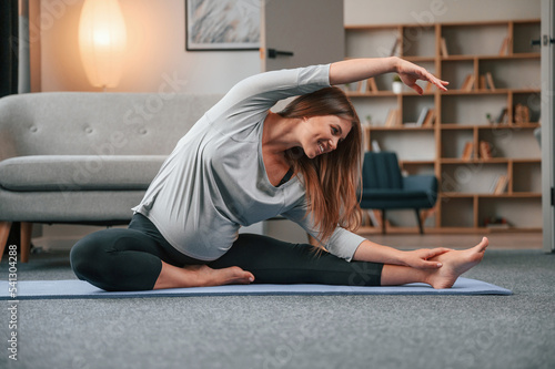 Doing yoga exercises. Beautiful pregnant woman is indoors at home