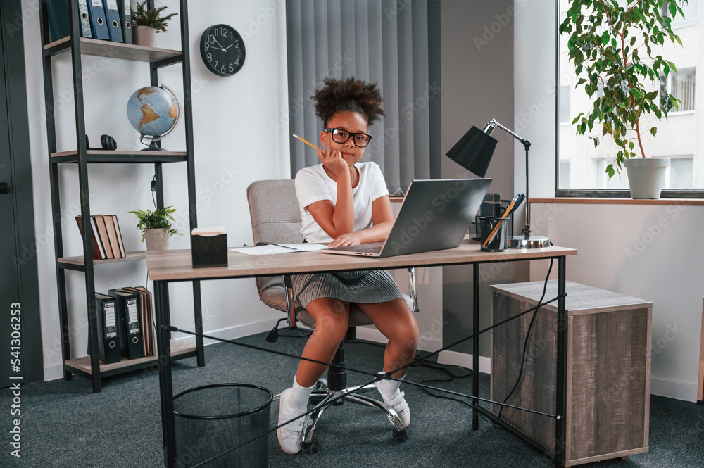 Sitting and looking at the camera. Cute female african american student child is indoors with laptop Sitting and looking at the camera. Cute female african american student child is indoors with laptop