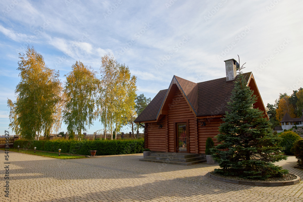 Panoramic view of a rural country house made of wooden beams and ornamental plants near a coniferous autumn forest.