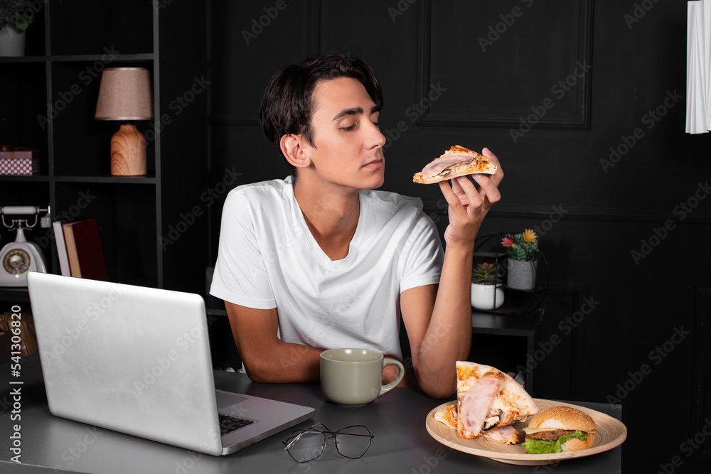 A young and funny guy is working in front of a laptop. Office work. A man in a black loft apartment. A young and funny guy is working in front of a laptop. Office work. A man in a black loft apartment.