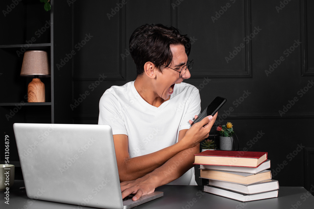 A young and funny guy is working in front of a laptop. Office work. A man in a black loft apartment. A young and funny guy is working in front of a laptop. Office work. A man in a black loft apartment.