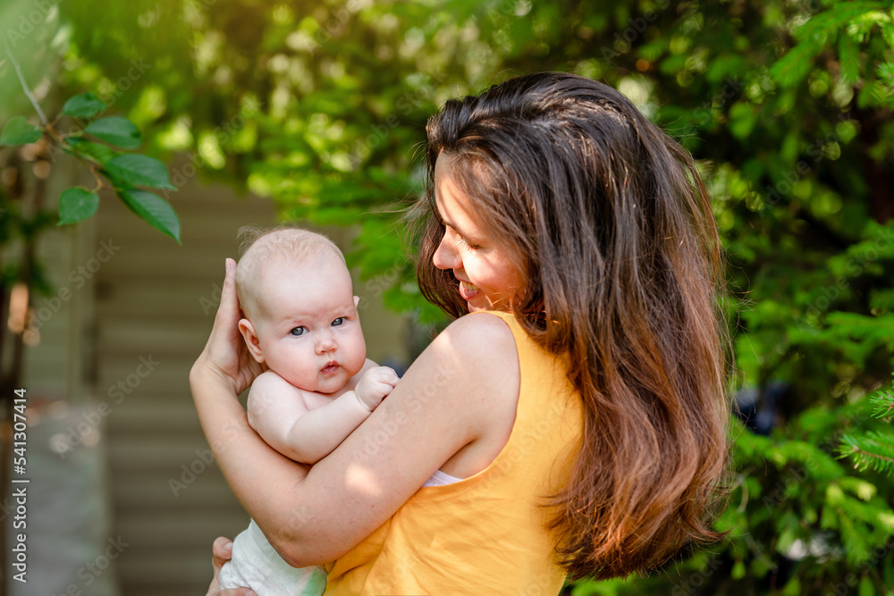 A young mother holds a baby in the park in the summer A young mother holds a baby in the park in the summer