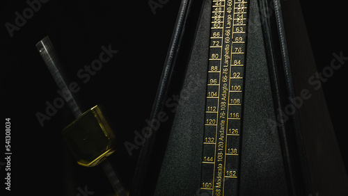 Mechanical metronome on a dark plain background: music, mechanical metronome, metronome, dark, black, background, isolated, gold, instrument, rhythm. photo