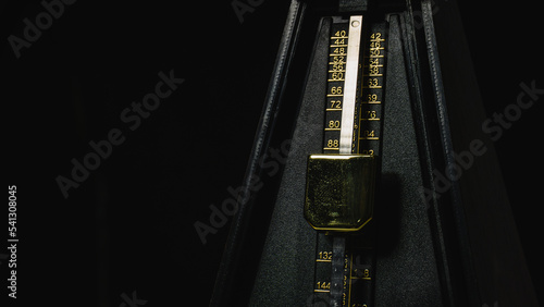 Mechanical metronome on a dark plain background: music, mechanical metronome, metronome, dark, black, background, isolated, gold, instrument, rhythm.