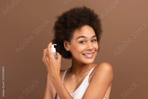 Cheerful young mixed race female applying gel on curly hair, make new haircut, looking at camera