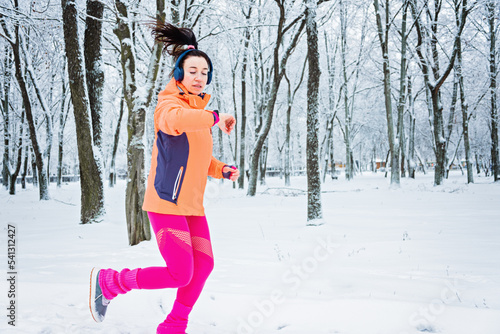 Running woman looking at smartwatch, checking heartrate and pulse during jogging in winter park. Fitness woman setting up smart watch for running training during winter workout