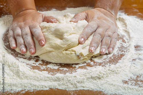 The hands of a Jewish woman knead the dough for challah for a festive meal on a wooden table.