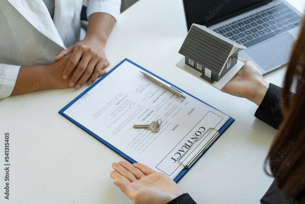 Have an Asian female real estate agent hold a house and key and explain a business contract, lease, purchase, mortgage, loan, or insurance to the woman who buys it. Have an Asian female real estate agent hold a house and key and explain a business contract, lease, purchase, mortgage, loan, or insurance to the woman who buys it.