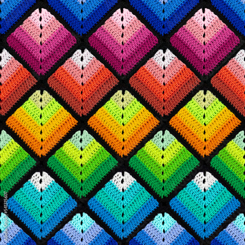 Seamless knitted pattern in the form of gradient rhombuses is crocheted with multi-colored threads. Patchwork style. Rainbow color combinations.