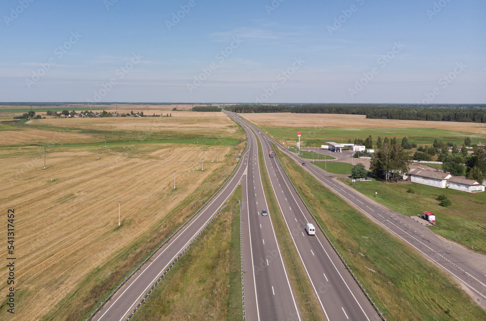 Top view of trucks and cars moving along the asphalt road along the fields.