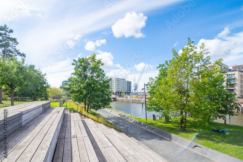 Wooden steps and seats invite you to rest in Baakenpark in Hamburg. The blue sky is streaked with clouds, the trees and meadows shine fresh green.