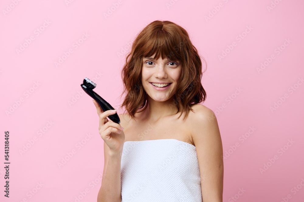 a happy, joyful, young woman stands with beautifully styled hair on a pink background and holds a black facial massager in her hand a happy, joyful, young woman stands with beautifully styled hair on a pink background and holds a black facial massager in her hand