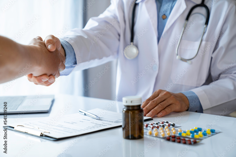Doctor and patient shaking hands in the office, they are sitting at desks, After the patient has successfully treated Doctor and patient shaking hands in the office, they are sitting at desks, After the patient has successfully treated