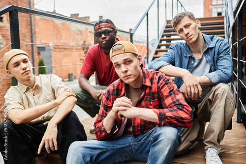 Diverse group of young guys wearing street fashion while posing on metal stairs in urban setting