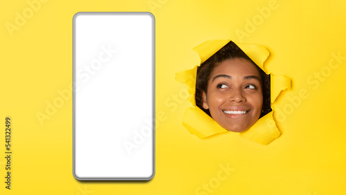 African Lady Peeking At Phone Through Hole On Yellow Background © Prostock-studio