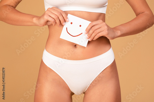 Women health concept. Lady in underwear holding paper with happy smiley face in hands near abdomen zone, cropped photo