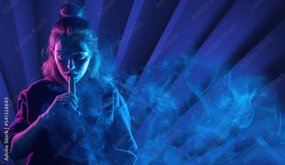Woman is engaged in vaping. Vape cigarettes. Young vaper woman on blue. Sale of devices for vaping. Vaper looks at camera through smoke. Buying e-cigs in vape shop. Vape shop concept. Woman is engaged in vaping. Vape cigarettes. Young vaper woman on blue. Sale of devices for vaping. Vaper looks at camera through smoke. Buying e-cigs in vape shop. Vape shop concept.