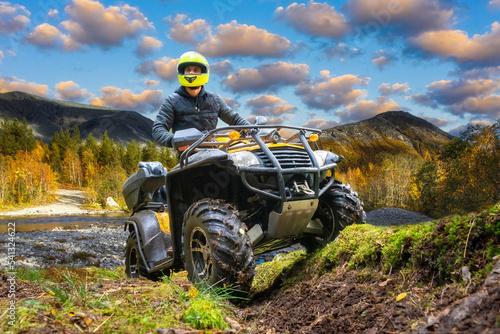 ATV rider man participates in motocross. ATV rides near forest. Man in yellow helmet for quad cycle. ATV rider in taiga. Off-road racing concept. Motocross in forest with river. Extreme sport on bike