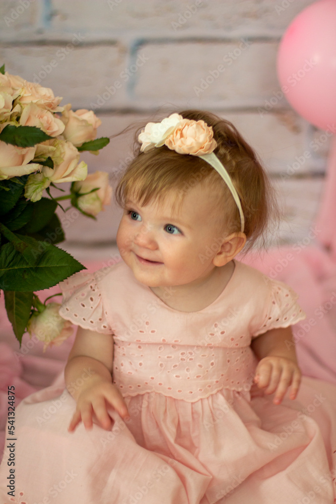 Fototapeta premium Pretty small girl with roses in beautiful dress sits and looks dreamy, beauty and fashion concept, indoor portrait against the backdrop of brick wall close-up. Beautiful little girl model .