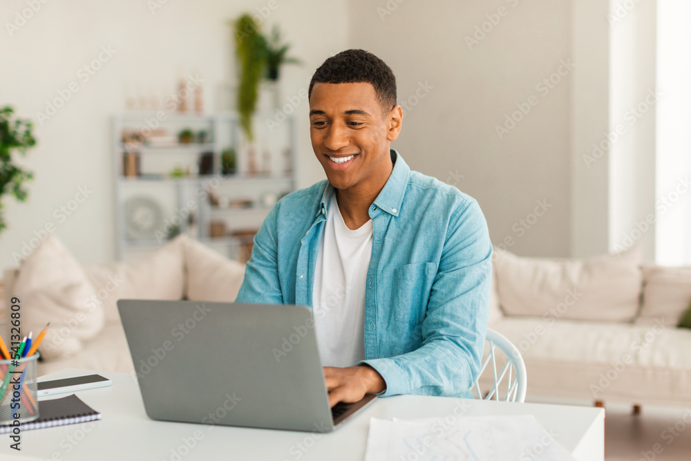Cheerful young handsome black guy manager in jeans working on laptop, has video call, online lesson Cheerful young handsome black guy manager in jeans working on laptop, has video call, online lesson