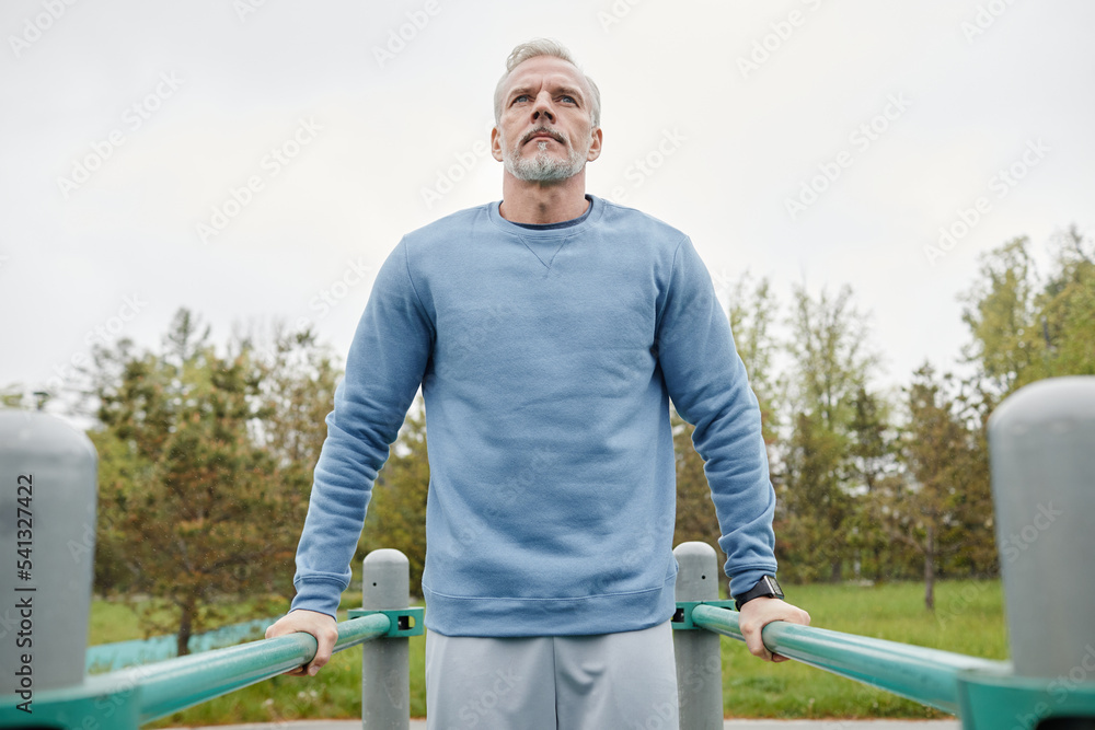 Fototapeta premium Low angle portrait of active mature man exercising on parallel bars outdoors, copy space