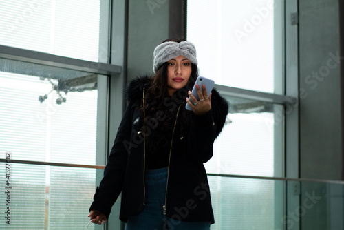 Latina girl is shopping in a mall, she looks at her cell phone to make a payment.