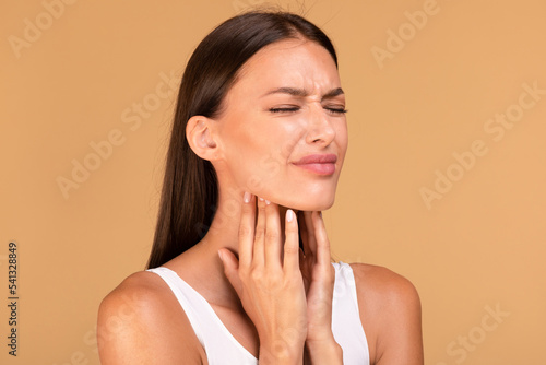 Cold symptoms and medicine concept. Portrait of sick woman suffering from sore throat, ill lady touching neck with hands photo