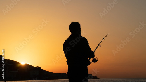 Silhouette of a standing man fishing at sunset in Turkey. Angler man holding fishing rod by the sea at evening. Leisure activity