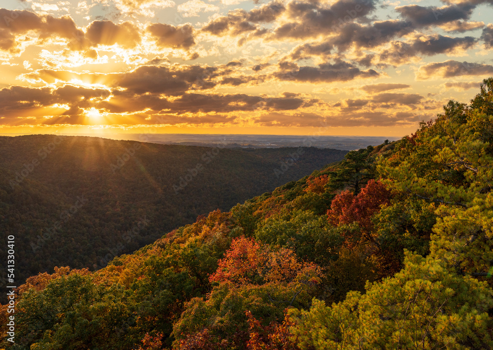 Sun setting behind clouds illuminating the fall colors of the trees in Coopers Rock State Forest