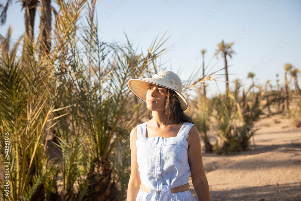 Tourist woman with hat walking through the desert landscape and palm trees that offers the city of Marrakech in its palm grove, this place is very visited in Morocco by tourists.