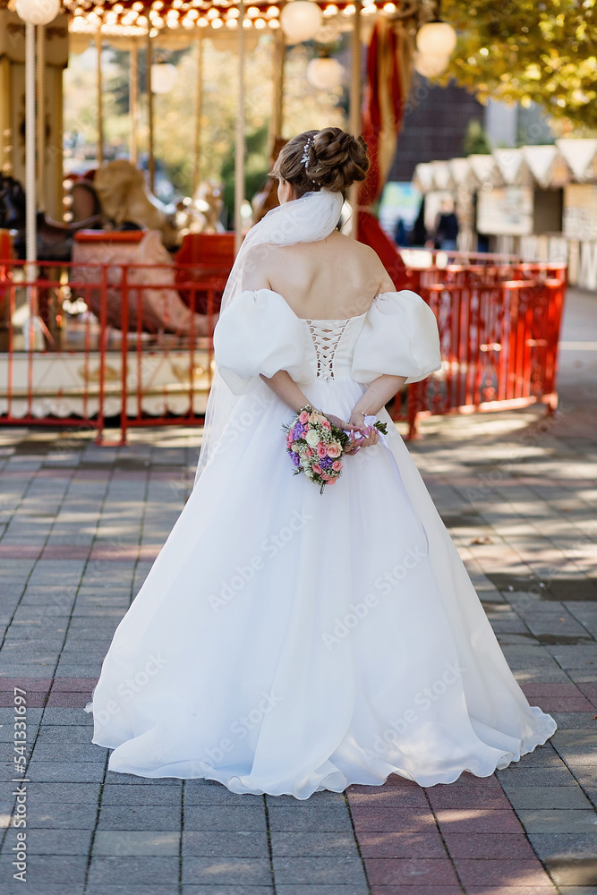 Rear view of the bride in a luxurious white wedding dress holding a bouquet. Wedding Details