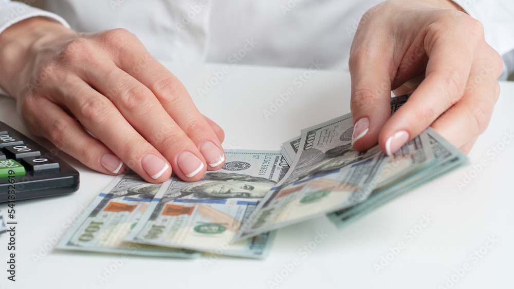 a man's hand holds out one hundred dollar bills against the background of an office table with a computer a man's hand holds out one hundred dollar bills against the background of an office table with a computer