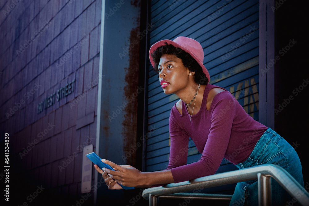 Young African American girl with short afro hair, wearing purple long sleeve T shirt, Denim skirt, pink hat, stands by doorway on street in New York City, reads blue tablet computer, thinking..