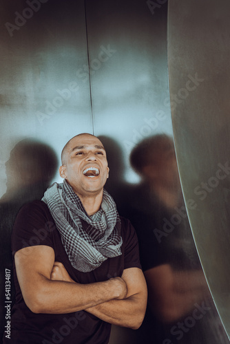 Obraz na płótnie Young man with shaved head, wearing black T shirt, long patterned scarf around neck, crossing arms, standing in corner, opening mouth, shouting. . w salonie