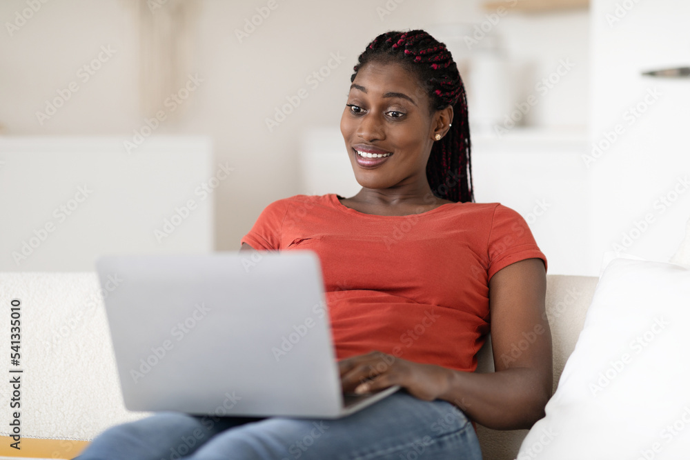 Online Communication. Smiling Young Black Woman Sitting On Couch And Using Laptop Online Communication. Smiling Young Black Woman Sitting On Couch And Using Laptop