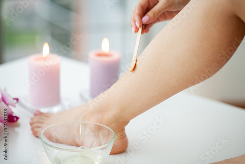 Close up woman applies wax to her leg to remove hair