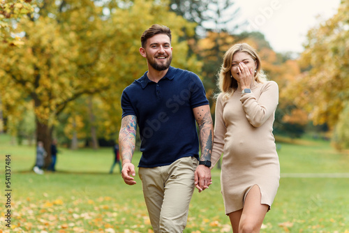 Young pregnant woman and her handsome husband are walking at the autumn park.