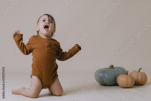 Cute small baby is staying near a pumpkins. Studio photography.