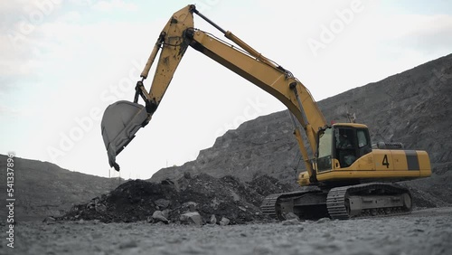 The excavator rakes the ore with the bucket, forming a pile. The action takes place in an open pit. 