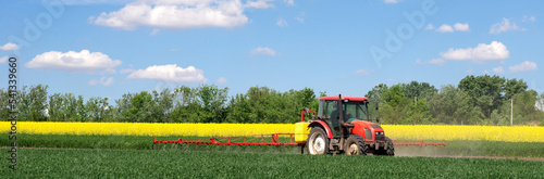 Tractor sprinkling pesticides on the agricultural field on a sunny spring day