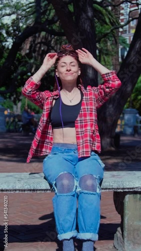 red haired girl with braids lying down on a bench in a square one sunny day	