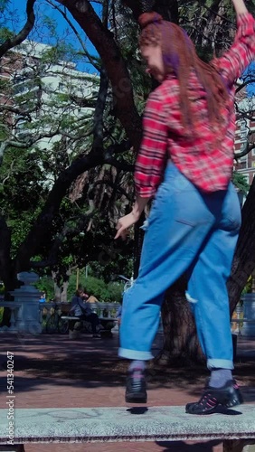 red haired girl with braids playing on a bench in a square one sunny day	