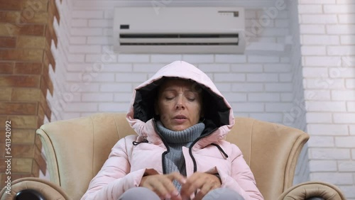 Lady shivering from the cold in flat. A view of a woman in winter jaket shivering in unheated room during winter Europe crisis. photo