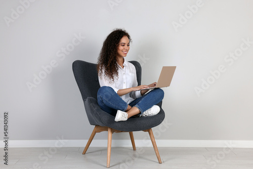 Canvas Print Young African-American woman working on laptop in armchair indoors